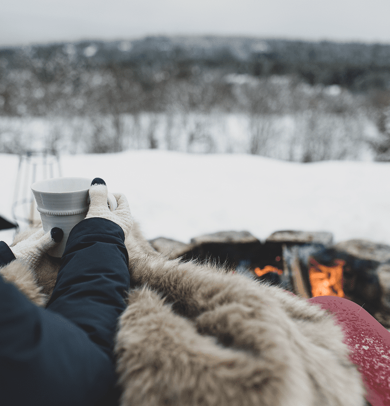 Hands holding mug by outdoor fire in snow